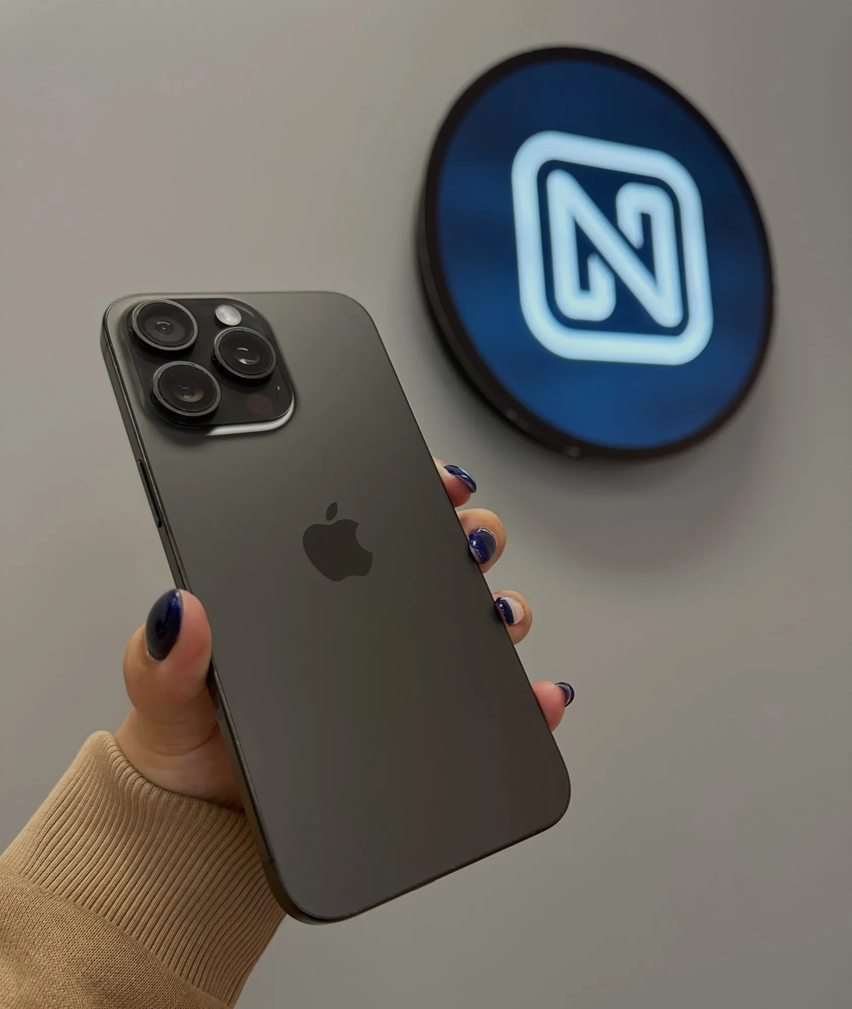 iPhone 15 Pro na mão, com o letreiro em neon da NaN ao fundo
